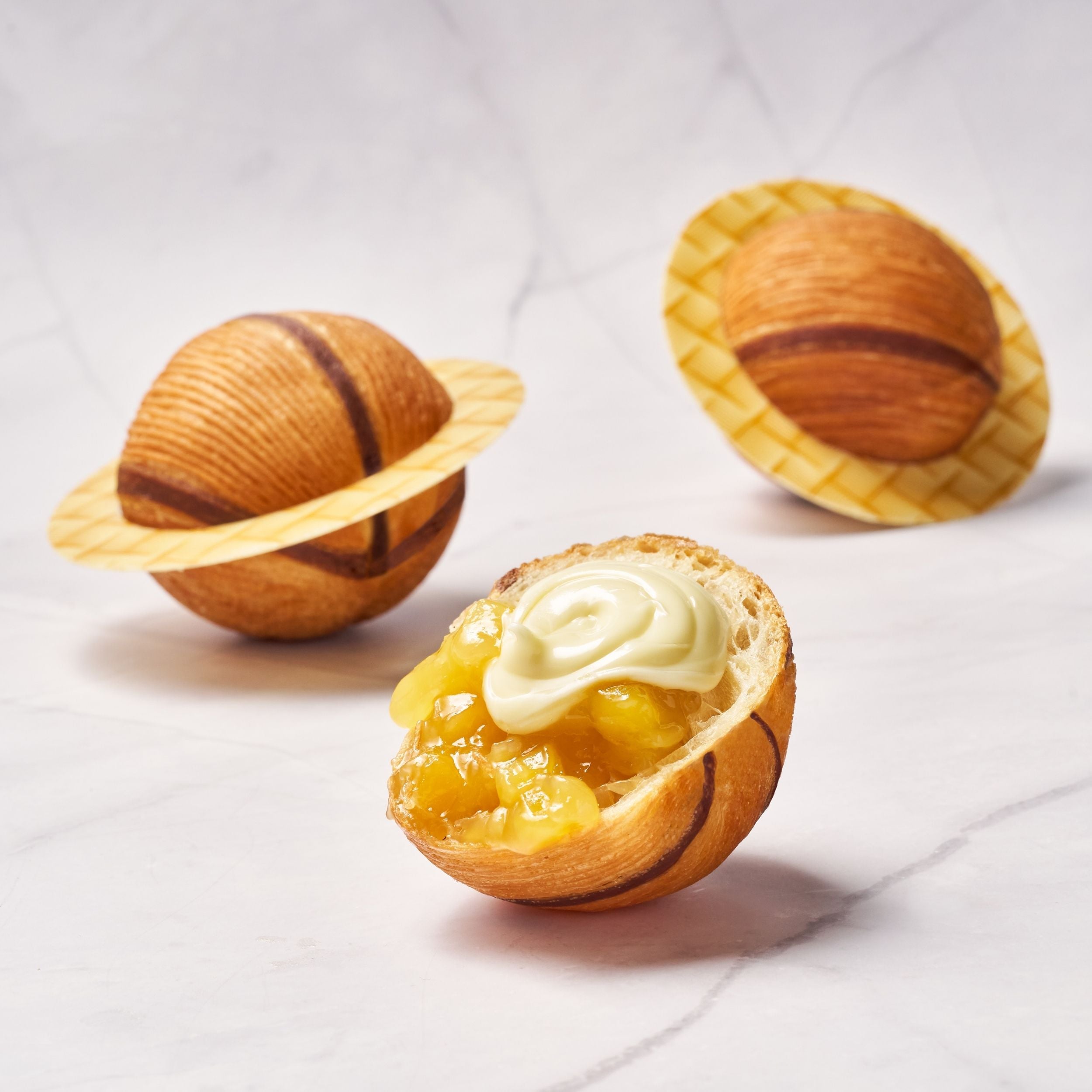 Croissant a sfera con righe al cacao con ripieno mango e crema al cocco decorato con decorazione di cioccolato come se fosse il pianeta saturno 